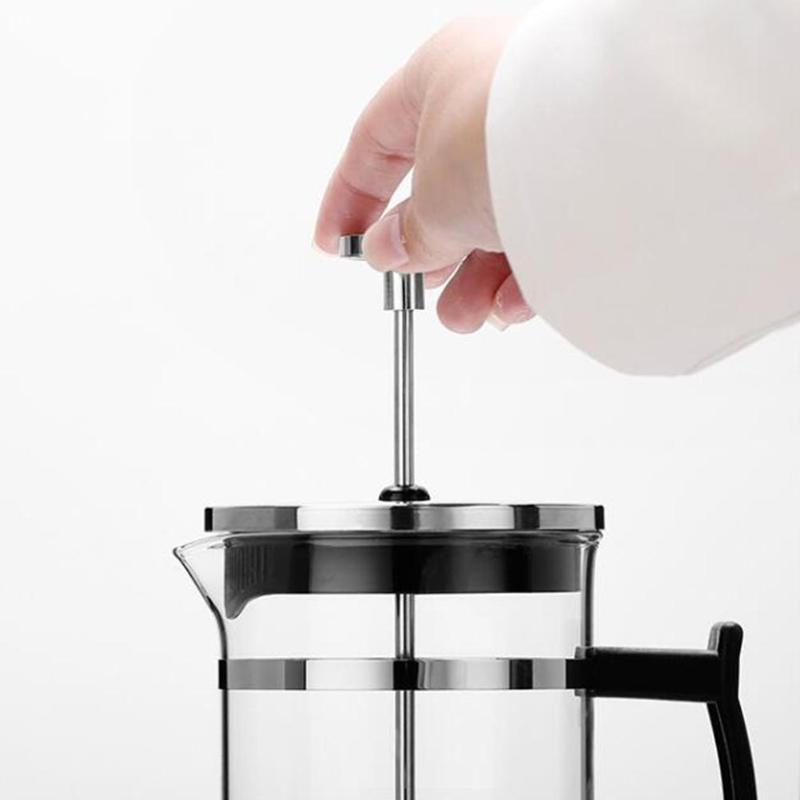 Modern French press coffee maker with heat-resistant glass, stainless steel accents, and sturdy black handle, emitting steam, placed on a marble slab.