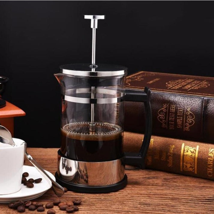 Stainless steel and glass French press coffee maker filled with rich coffee, elegant black handle, placed on a dark wooden surface near coffee beans